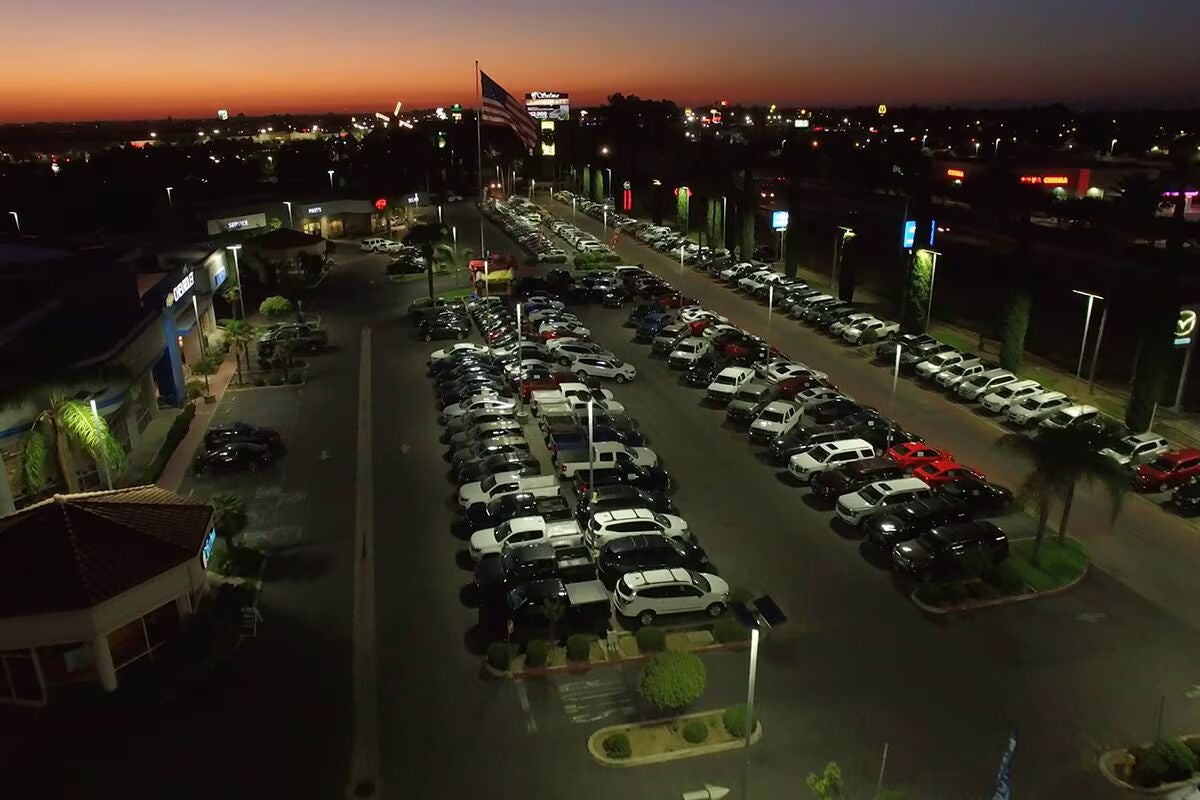 Aerial view of a car dealership at dusk. Rows of cars fill the parking lot under a sunset-colored sky.